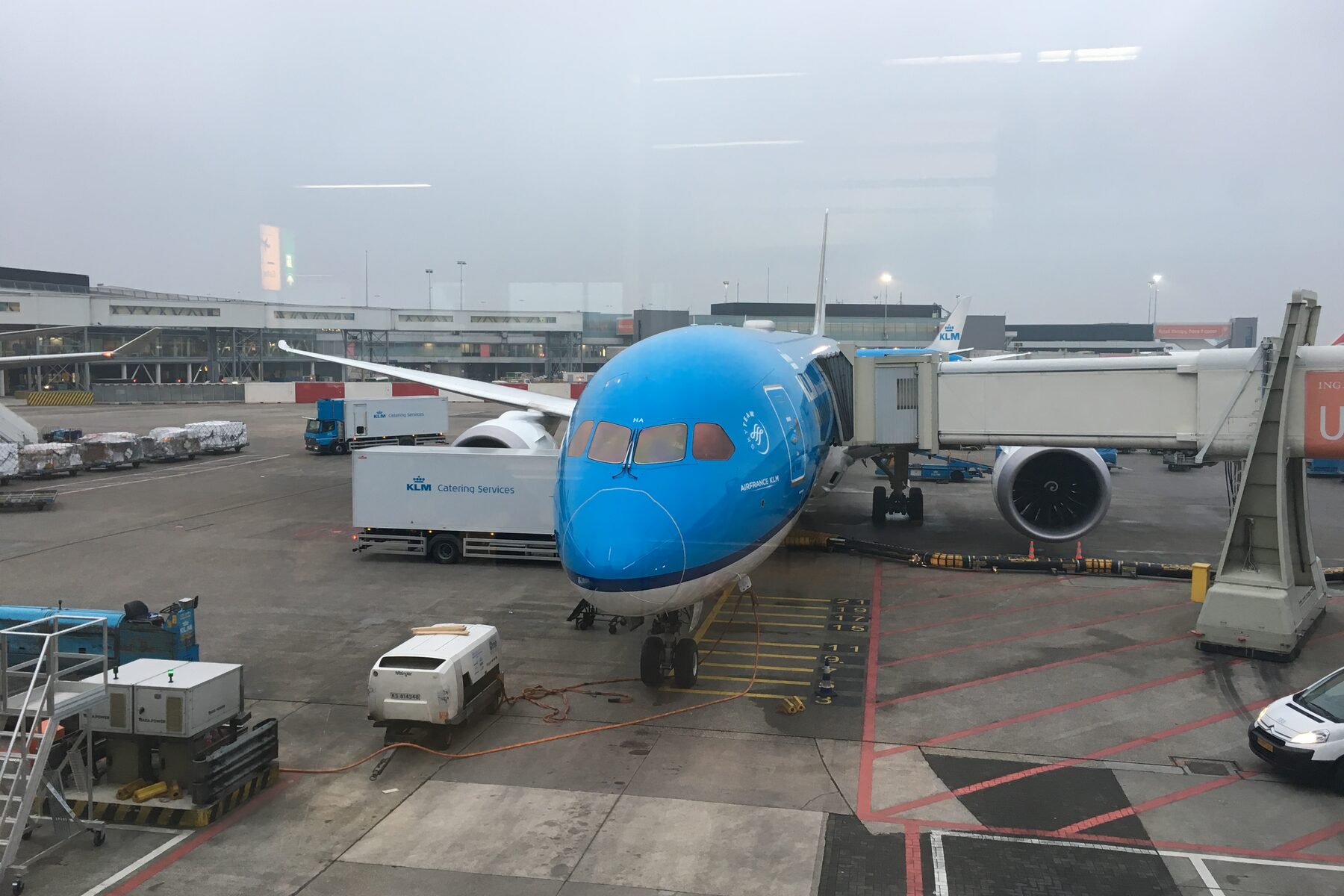 A KLM aircraft at an airport gate with a jet bridge on an overcast day.