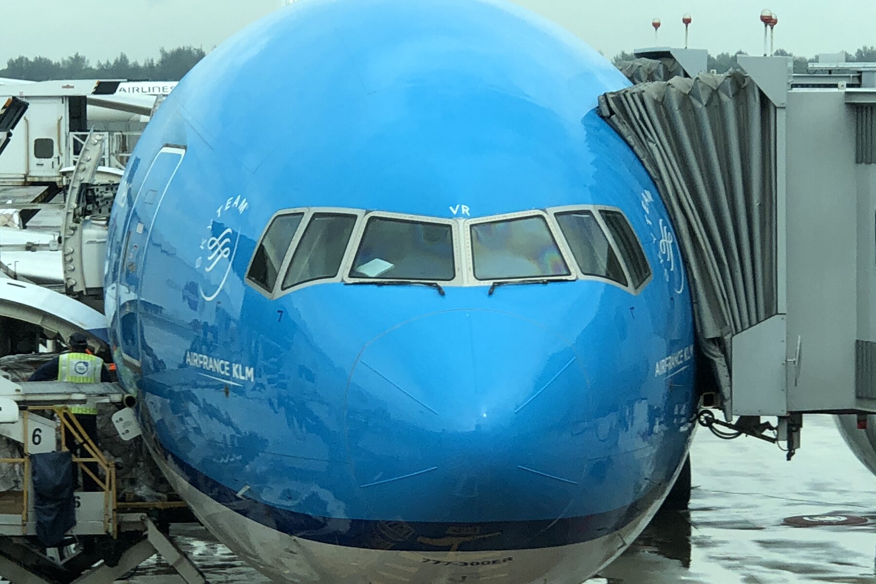 The nose of a KLM wide-body aircraft at a boarding gate with a jet bridge connected.