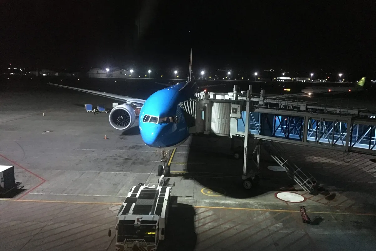 An aircraft parked at a gate at dusk with a jet bridge connected and ground equipment alongside.