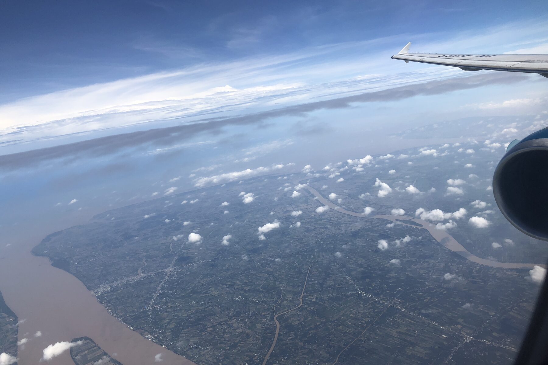 Aerial view of farmland and a river from an aircraft window at cruising altitude.